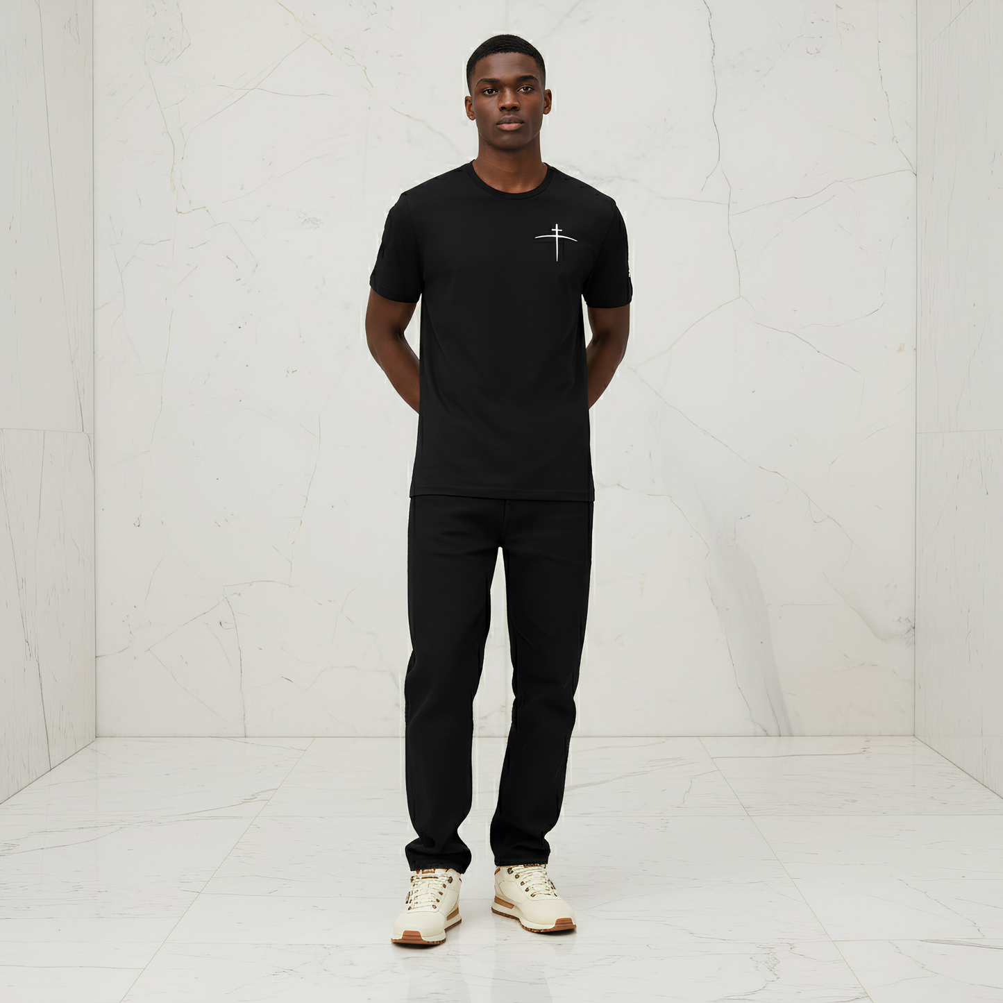 Man wearing a black t-shirt with a logo and black pants in a white room