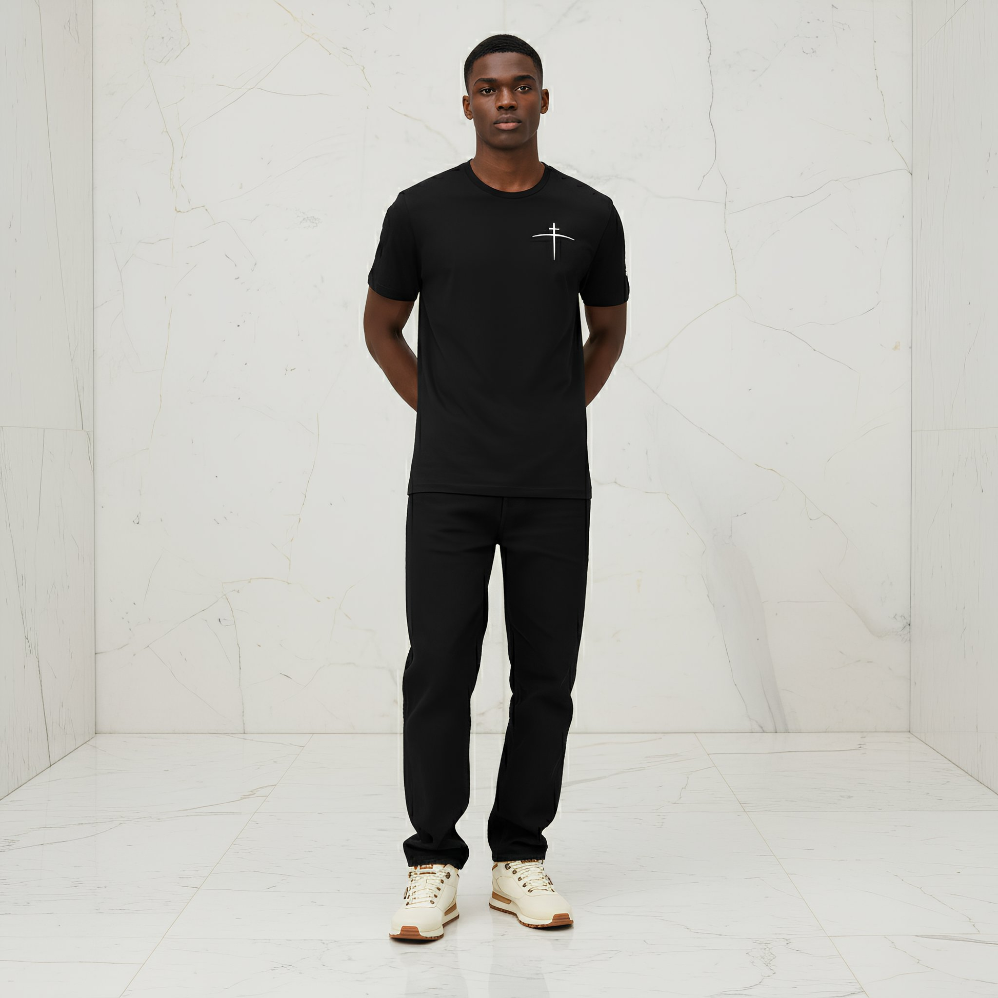 Man wearing a black t-shirt with a logo and black pants in a white room